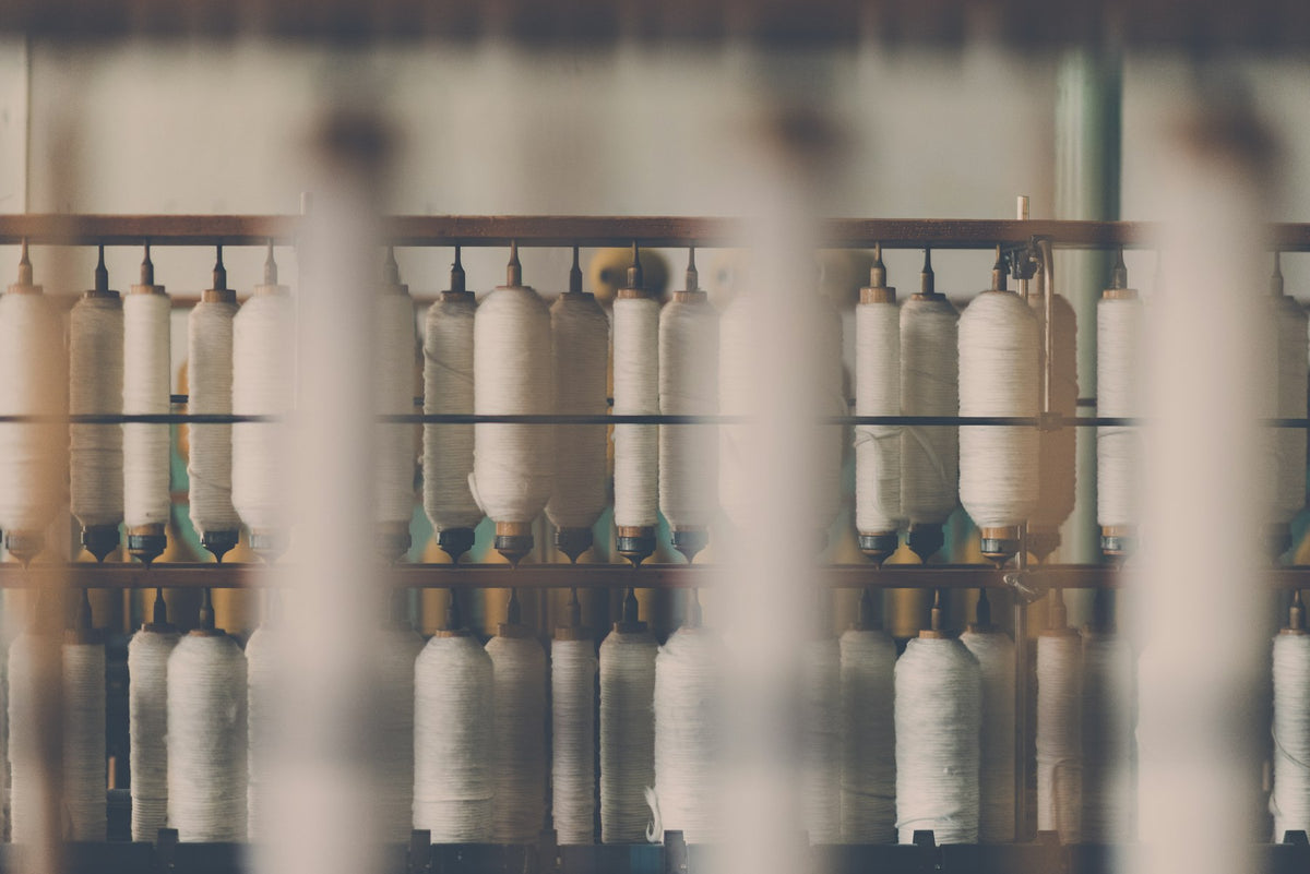 Rows of white cotton thread spools on a wooden rack in a textile mill