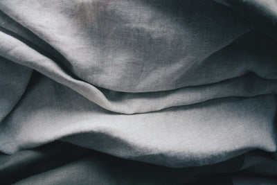 Folded natural linen fabric in soft neutral tones, showing the weave texture up close