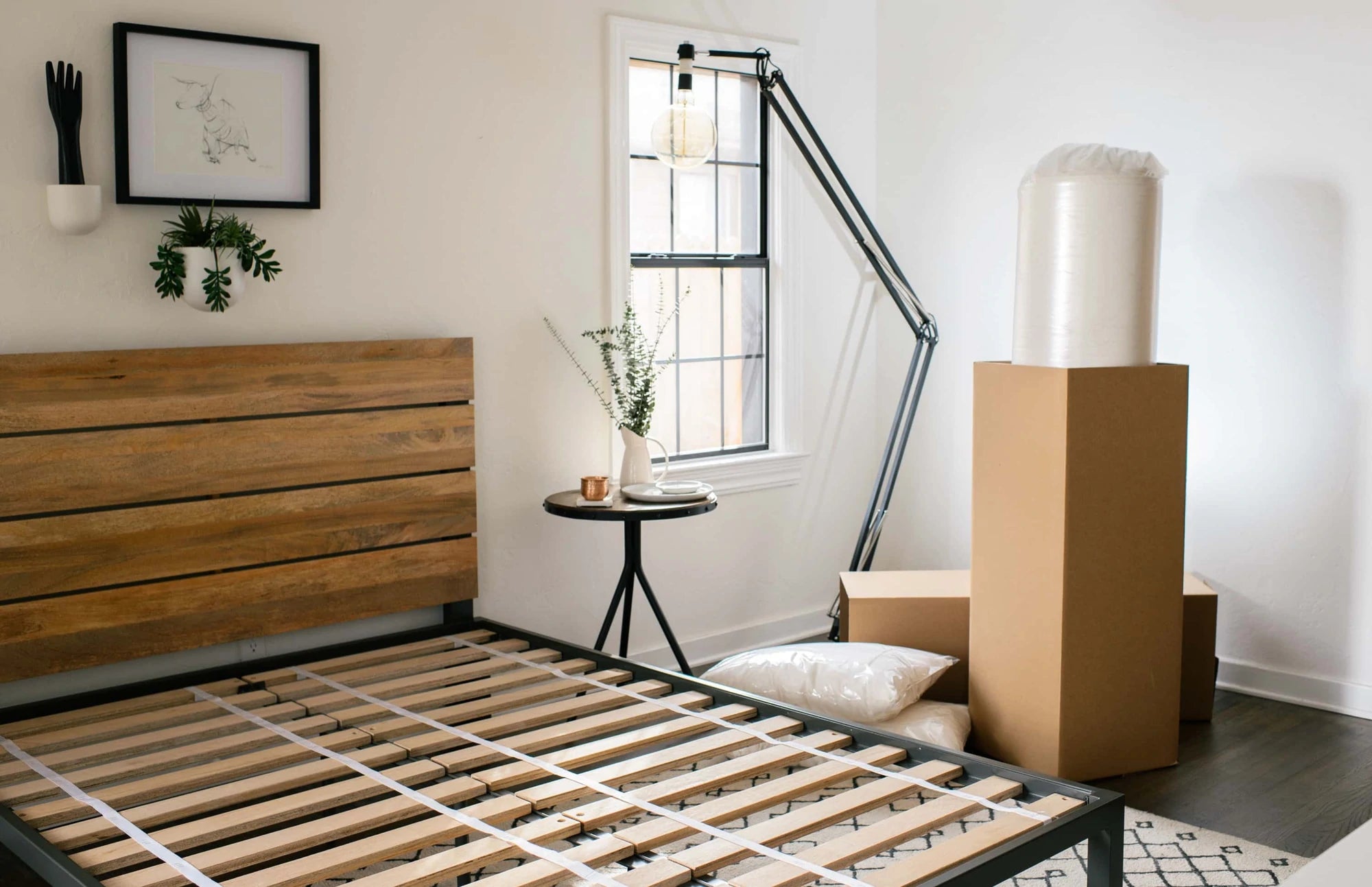 Bed frame before a mattress is placed on it. Organic latex mattress arrived by mail and is roll-packed in a box next to the bed.